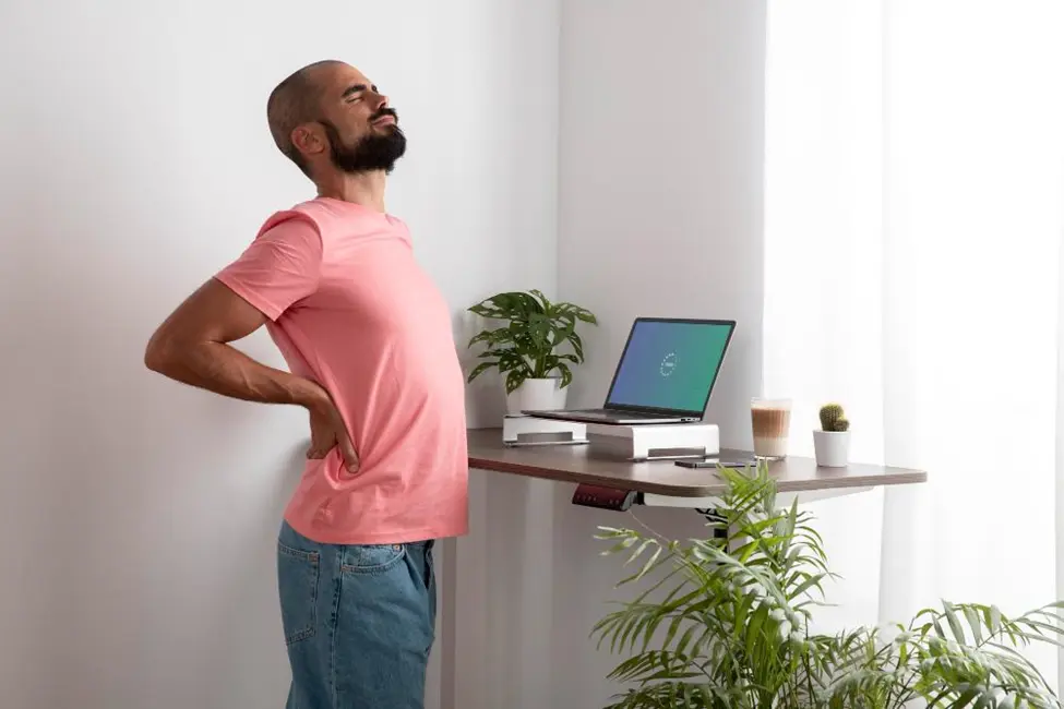 Man standing behind work station with back pain holding his lower back
