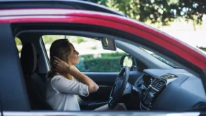 Woman sitting in car holding neck due to whiplash injury after accident