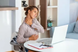 Woman at desk holding neck due to fibromyalgia-related pain