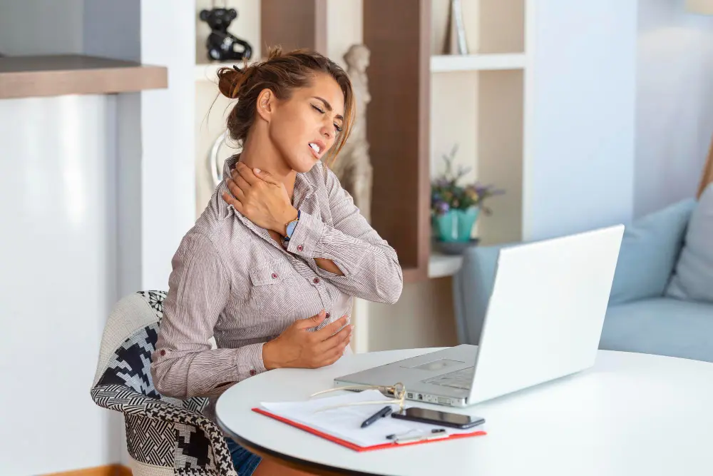 Woman at desk holding neck due to fibromyalgia-related pain